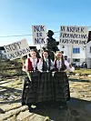 Bildet viser Heidi Lysgård Fagerheim, Elise Antonsen Lura og Lotte Bjerknes Skram kledd i bunader. De holder skilt der det står «stopp galskapen», «nok er nok» og «vi krever fødeavdeling i Kristiansund». De tre bor på Veiholmen på øya Smøla. De får aller lengst vei å dra om fødeavdelingen i Kristiansund stenges.