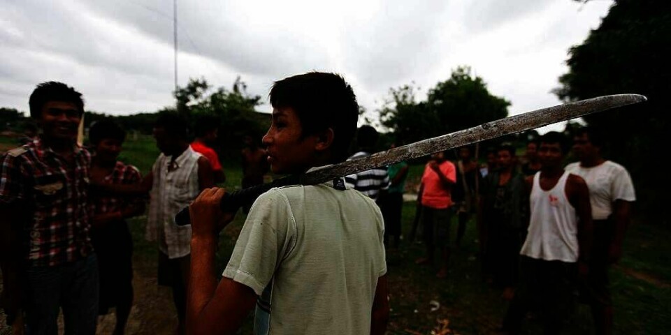 KAMPER: En mann går med machete for å beskytte hjemmet sitt i Rakhine i Myanmar. Nå har myndighetene bestemt at det er unntakstilstand vest i landet.