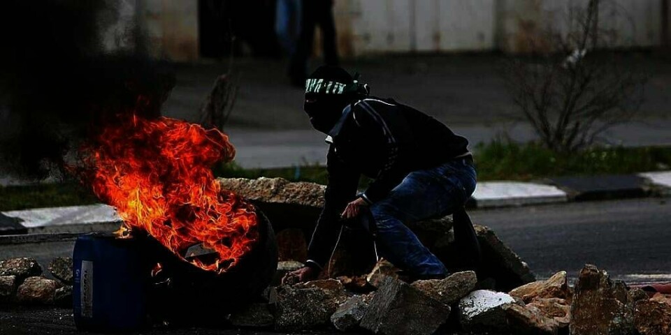 SINT: En palestinsk demonstrant gjemmer seg for israelske soldater. Søndag protesterte mange palestinere. Årsaken er at en palestinsk fange trolig ble torturert til døde av Israel.