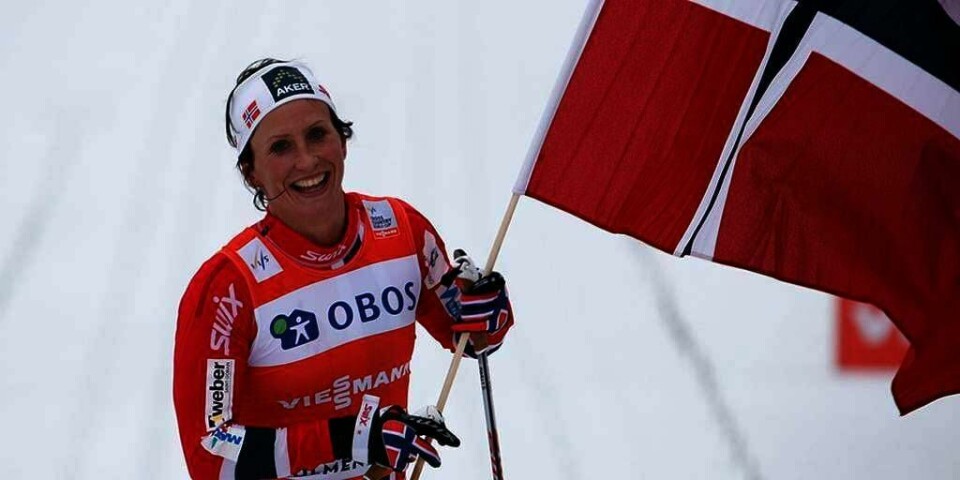 JUBLET: Skiløper Marit Bjørgen vant tremila i Holmenkollen i Oslo søndag. Neste helg kan hun vinne verdenscupen i langrenn sammenlagt. Bildet viser en skiløper som smiler og veiver med et norsk flagg. Marit Bjørgen vant tremila i Holmenkollen i Oslo søndag. Neste helg kan hun vinne verdenscupen i langrenn sammenlagt.