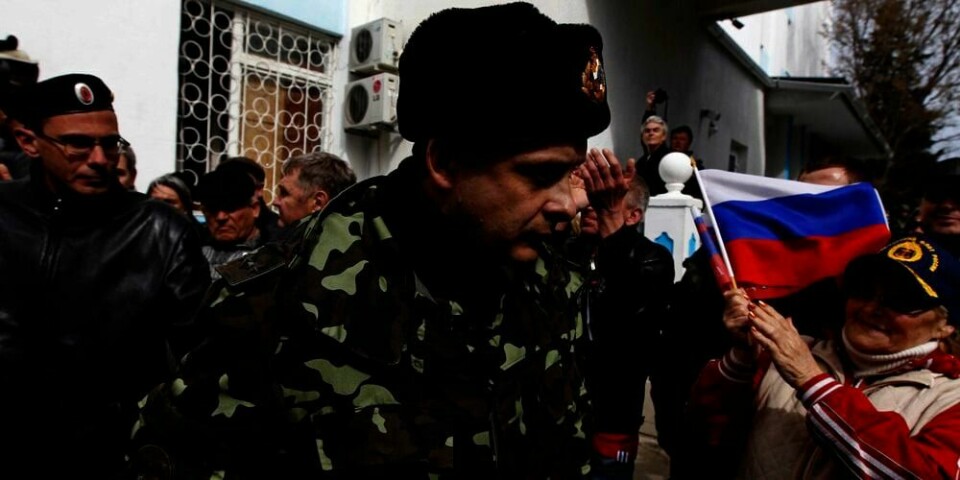 FLAGG: En ansatt ved marinebasen i Sevastopol på Krim går forbi grupper som støtter Russland. Onsdag kom rundt 200 personer som støtter Russland inn på Ukrainas marinebase i byen Sevastopol. Gruppa heiste tre russiske flagg.