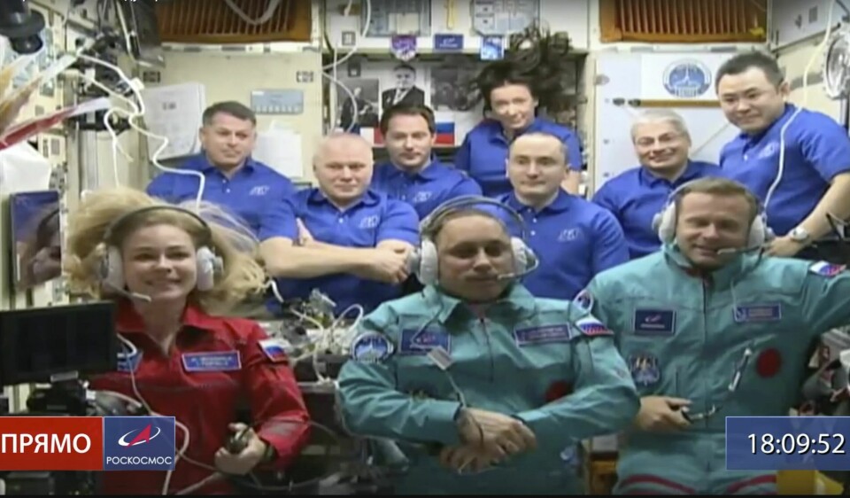 FILM: Julia og Peresild og Klim Shipenko har reist fra jorda for å lage film. Her er de på Den internasjonale romstasjonen ISS. In this photo taken from video footage released by Roscosmos Space Agency, actress Yulia Peresild, left, film director Klim Shipenko, right, and cosmonaut Anton Shkaplerov sit in the first row among other participants of the mission in the International Space Station, ISS, Bildet er av folk på den internasjonale romstasjonen. I bakgrunnen står mannskapet som pleier å være der. I forgrunnen er skuespilleren Julia Peresild, regissøren Klim Shipenko og kosmonauten Anton Sjkaplerov. Foto: Roskosmos / AP / NTB