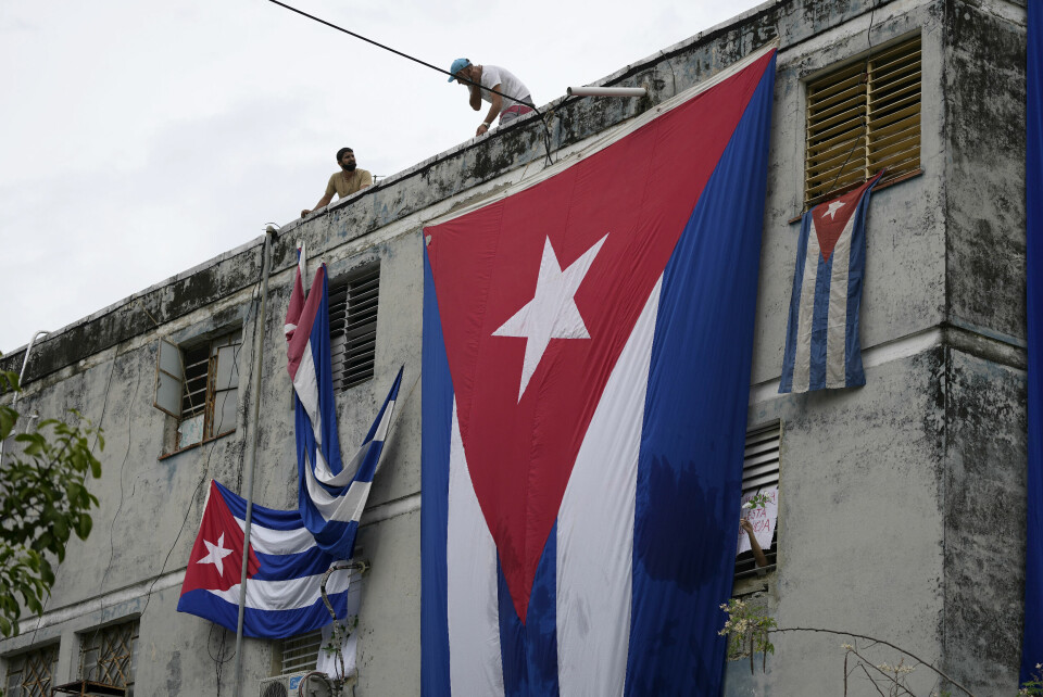 HVIT ROSE: Et flagg ble heist over vinduet til aktivisten Yunior Garcia Aguilera. Det skjedde da han holdt en hvit rose ut av vinduet. Cubanske flagg henger flagg foran vinduene der aktivisme Yunior Garcia Aguilera bor i et forsøk på å hindre ham fra å kommunisere med omverdenen. Foto: Ramon Epinosa / AP / NTB