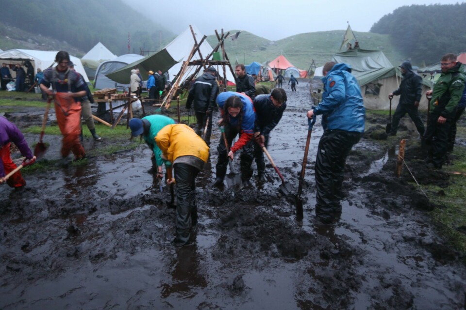 OVERSVØMMELSE: Mye regn har gjort om leirplassen til landsleiren Gnist 2022 for speiderne i Norges KFUK-KFUM-speidere om til en gjørmeleir. Speidere fra flere grupper evakueres. Folk fra hele leiren bidrar med å få bort vann og grave grøfter. Bildet viser folk som graver grøfter i en av leirgatene som er fylt med vann og gjørme.