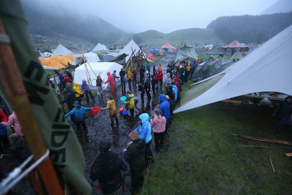 REKKER:Speidere sender bøtter fra person til person. Slik får de tømt områder for vann på den overfylte speiderleiren. Vannet tømmes i elva rett ved. Bildet viser folk som sender bøtter fra person til person med gjørmevann.