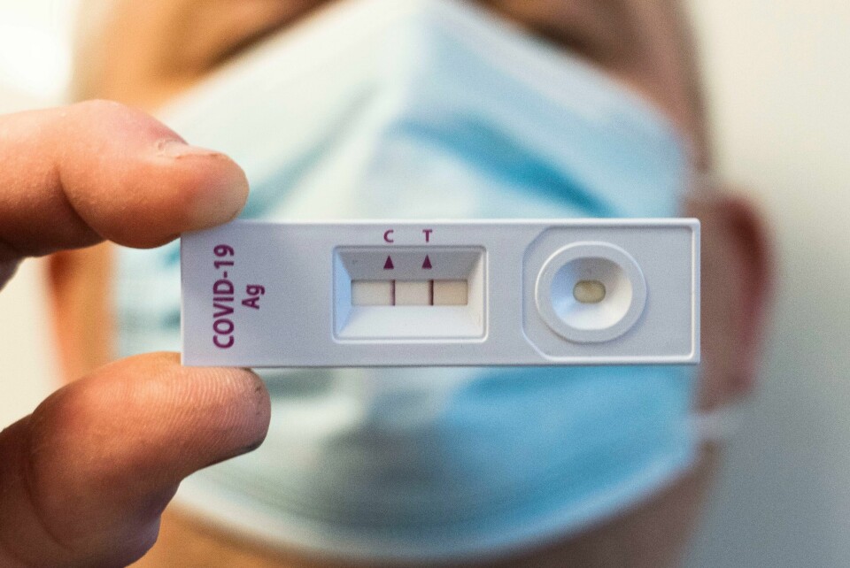 LENGE: Noen av dem som får korona, blir syke lenge. Også etter at de er friske fra korona. Det blir ofte kalt long covid. Bildet er av en person med munnbind som holder opp en hjemmetest for korona. Testen viser spor av smitte. Foto: Erik Johansen / NTB