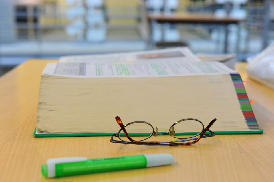 UTDANNING: Mange innvandrere tar høyere utdanning. Men fire av ti ender med å jobbe i et yrke de er overkvalifisert til.Foto: Bildet viser en pensumbok, briller og en tusj på en lesesal ved et universitet.