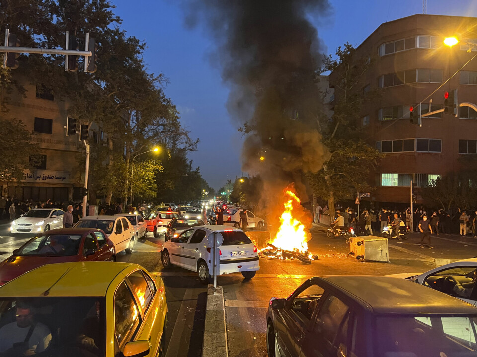 PROTESTER: En politi-motorsykkel brenner under en protest i Teheran i Iran. Ein motorsykkel står i brann i samband med ein protest mot at ei ung kvinne døydde i varetekt etter å ha vorte arrestert av moralpolitiet i Teheran. Foto: AP / NTB