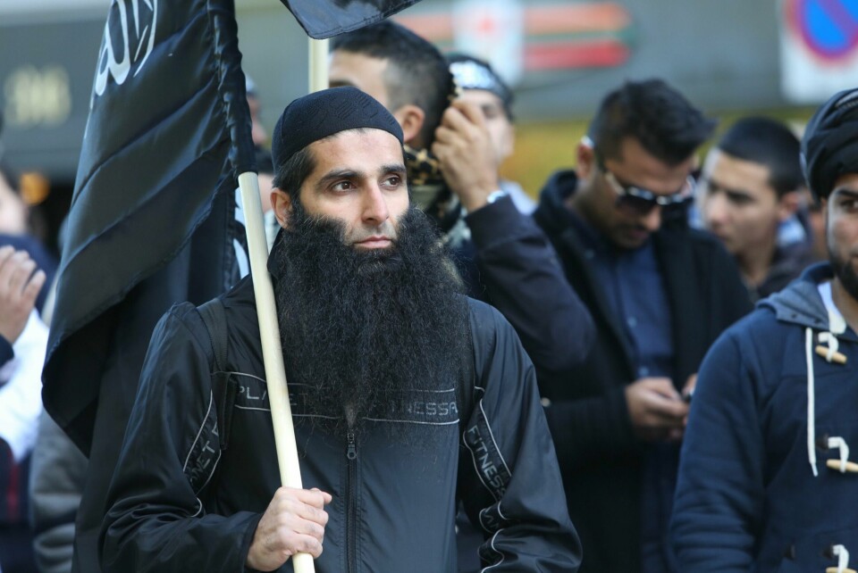 ARREST: Arfan Bhatti skal være i arrest i Pakistan. Han skal ha blitt anholdt av en del av politiet som jobber med anti-terror. Bildet er av blant annet Arfan Bhatti som protesterer foran den amerikanske ambassaden i Oslo. Han har på en grå og svart treningsjakke, og holder et svart flagg med hvit arabisk tekst. Foto: Kyrre Lien / NTB