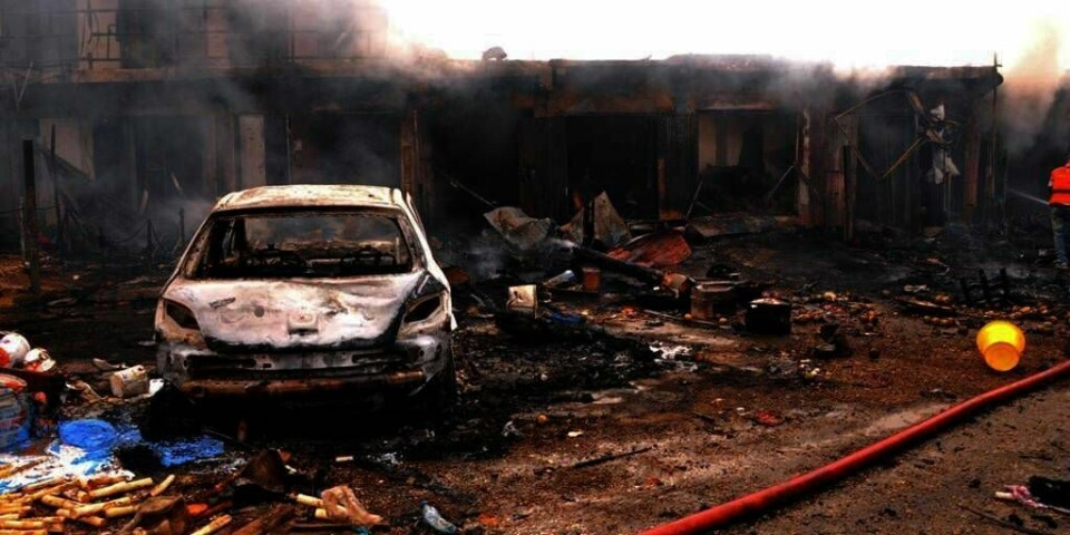 EKSPLOSJON: Vraket av en bil står foran en brennende butikk i byen Jos i Nigeria. Minst 118 mennesker ble drept da to bilbomber eksploderte mandag. Flere mistenker at islamistgruppa Boko Haram er skyld i angrepet.