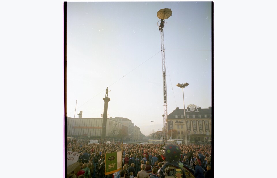 1977: Paraden endte alltid på torget i sentrum av Trondheim. Her klatret sjefen for Samfundet opp i et tårn. Tårnet skulle være høyere enn statuen av Olav Tryggvason. Her ser det ekstra høyt ut på grunn av vinkelen. I bakgrunnen vinker UKAs styre til balkongen på Phoenix hotell. Bildet viser tårnet som UKA-studentene laget på torget i 1971. Studentene samler seg på torget.