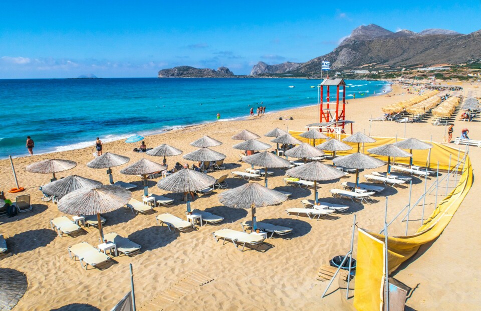 KRETA: Du må i karantene når du kommer hjem fra øya Kreta. Flere land er nå blitt røde eller oransje. Bildet er av parasoller og solsenger på en strand. Det er blått hav. Bildet er fra Falasserna på Kreta i Hellas. Foto: Halvard Alvik / NTB