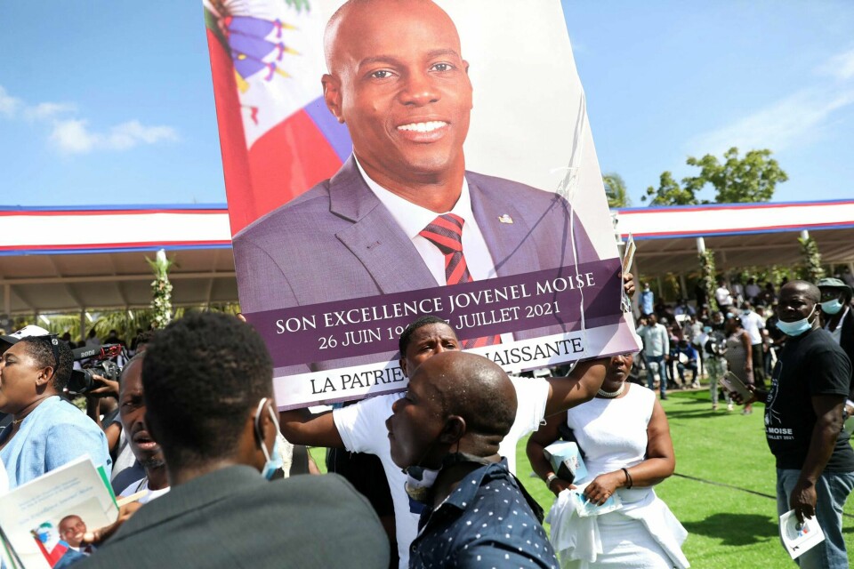 SORG: Mange folk i sorg samlet seg under begravelsen til Jovenel Moïse. Nå er folk bekymret for at de aldri vil få svar på hvorfor presidenten ble drept. Bildet er av folk som står utenfor begravelsen til president Jovenel Moïse i Haiti. I midten av bildet er en stor plakat med bilde av presidenten. Foto: Valerie Baeriswyk / AFP / NTB