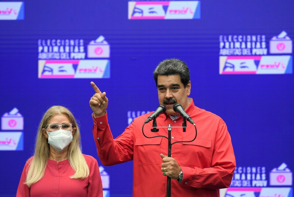 MØTER: Det skal være nye møter mellom regjeringen til Nicolás Maduro og opposisjonen. Bildet er av Venezuelas president Nicolás Maduro som snakker på en pressekonferanse. Han står bak et mikrofonstativ med to mikrofoner. Han er foran en blå vegg og har rød skjorte. Han har sort hår og bart. Ved siden av står en blond kvinne med briller og munnbind. Hun har på seg en rød trøye. Foto: Matias Delacroix / AP / NTB