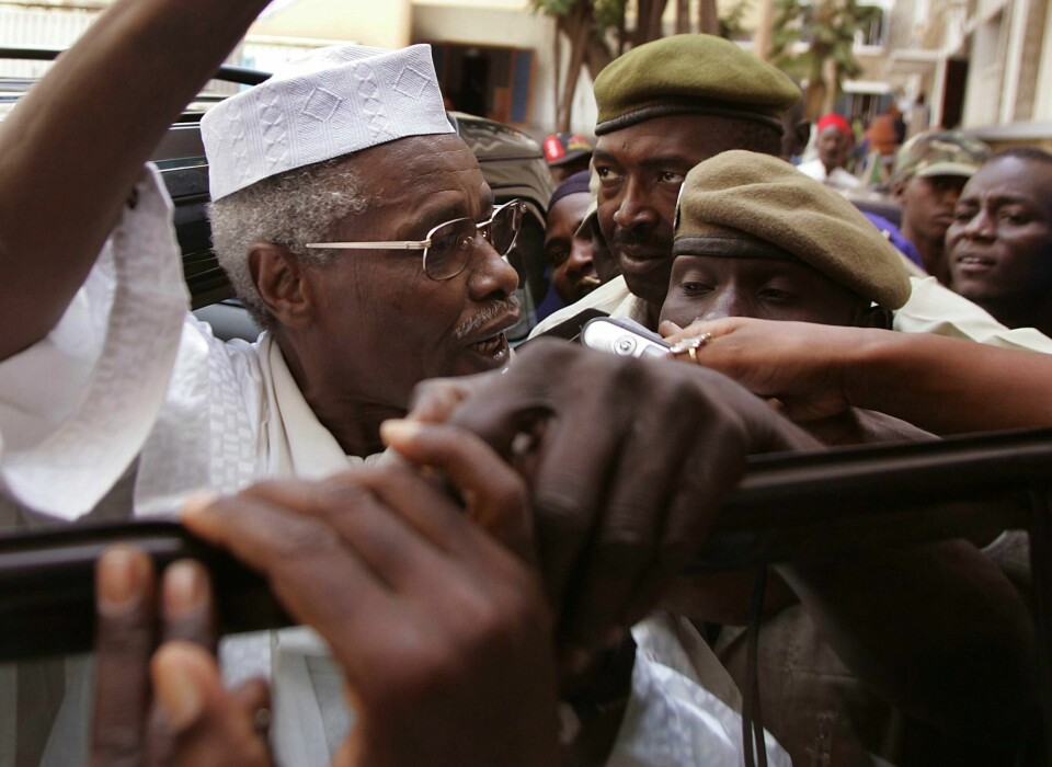 DØD: Hissène Habré var diktator i Tsjad fram til 1990. Nå er han død. Bildet er av Hissène Habré i 2005. Han er på vei ut av en domstol og ut i en folkemasse. I bakgrunnen står det soldater. Habré har på hvite klær, hvit hatt og briller. Foto: Schalk van Zuydam / AP / NTB