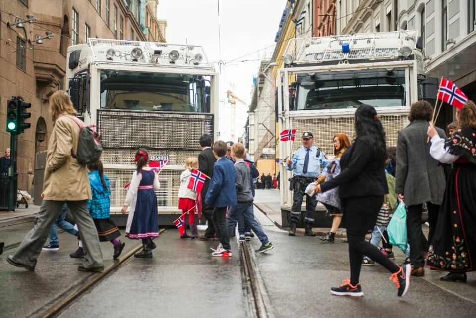 SIKKERHET: Politifolk passet på at ingen kunne kjøre på toget. De viftet også med flagg og hilste på barn. Bildet viser to store lastebiler med gitter foran. De sperrer en sidegate til Karl Johan. Foran bilene står politifolk med flagg. Foran dem går barnetoget.
