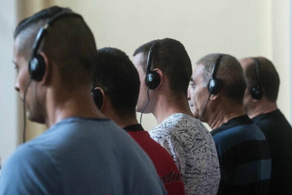 DRAP: 11 menn må i retten etter at 71 flyktninger ble kvalt i en lastebil. Her sitter fem av mennene med høretelefoner. De for oversatt det som blir sagt på i retten.