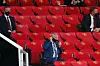 Bildet er fra fotball-stadion Old Trafford i Manchester. Logoen til Manchester United er på setene. Flere menn sitter langt fra hverandre med munnbind. En av de er den tidligere treneren til Manchester United, sir Alex Ferguson.
