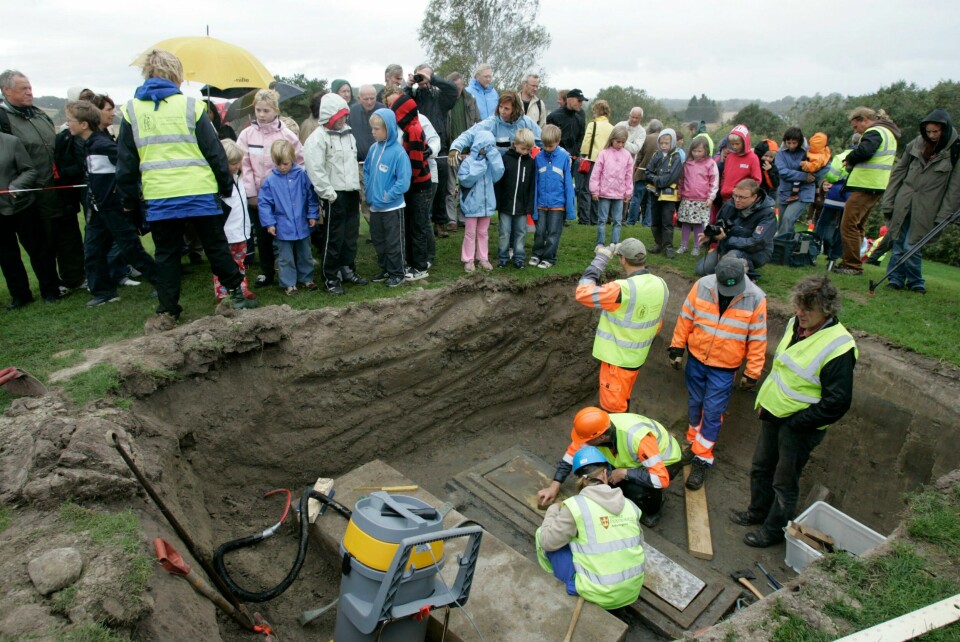 UNDERSØKT: Forskere har undersøkt DNA fra skjeletter fra flere viking-graver. Det gjør at de kan si mer om hva som var en typisk viking, og hvordan han eller hun så ut. Bildet er fra forskere åpnet Oseberg-haugen i 2007. Der fant de to kvinner i graven. Bildet er av flere personer som står nede i en viking-grav som de har åpnet. Det står barn på kanten av hullet som er gravd ut. De har funnet en kiste.