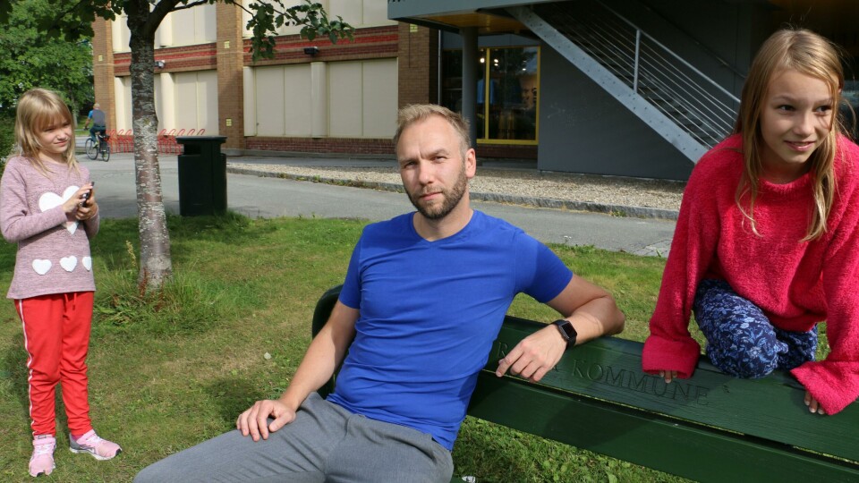 IMOT: Ørjan Kulseng-Johansen liker ikke den nye storskolen. Her er han med døtrene på ti og åtte år. Bildet viser Ørjan Kulseng-Johansen som sitter på en benk mens døtrene leker rundt ham.