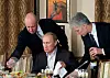 Bildet er av tre personer ved et bord med mat inne i en restaurant. Jevgeny Prigozjin eier restauranten og står til venstre i bildet. Vladimir Putin sitter ved bordet. Bildet er fra 2011. Foto: Misha Japaridze / AP / NTB