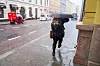 Bildet viser en dame som går med paraply i styrtregn.