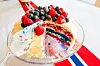 På bildet ser vi en kake med farger i det norske flagg. Det er en marsipankake med fargerike bær.