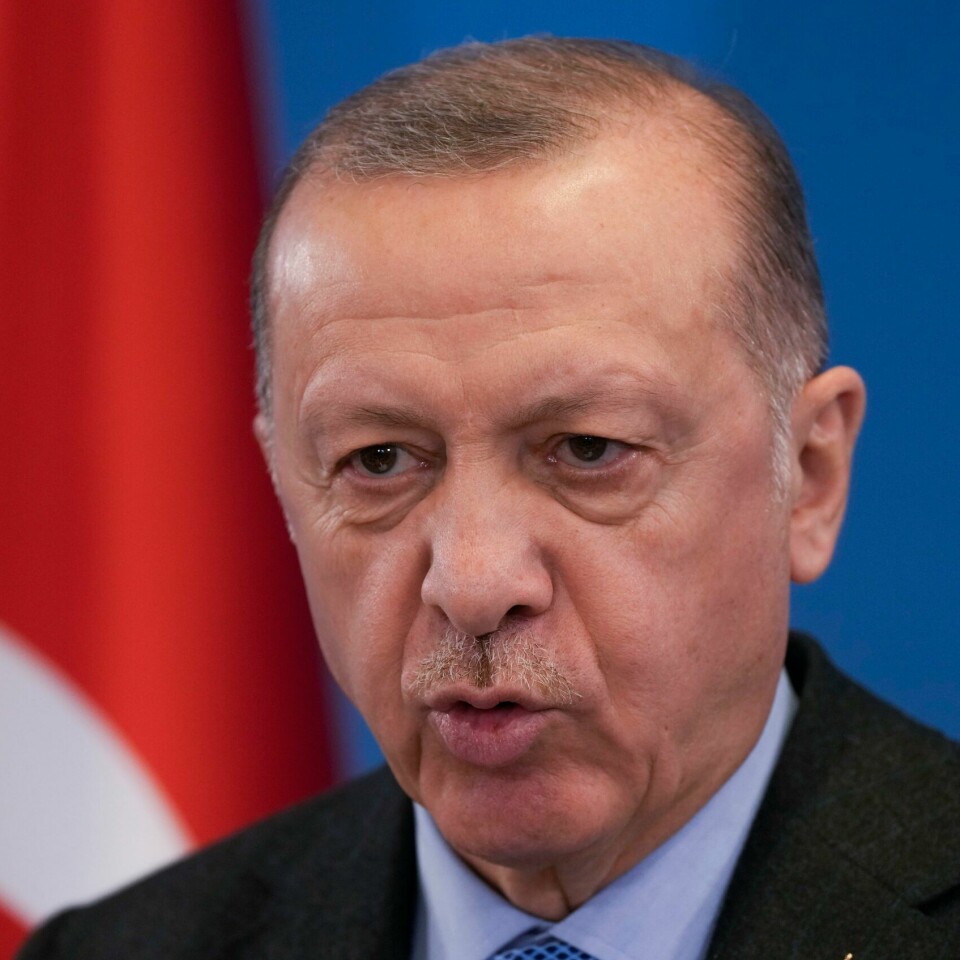 NEI: Erdogan er negativt til svensk og finsk medlemskap i Nato. Bildet er et nærbilde av Recep Erdogan. Han står foran en blå vegg. I bakgrunnen er et tyrkisk flagg. Det er rødt, med en hvit halvmåne og stjerne. Foto: Markus Schreiber / AP / NTB