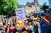 Folk går i Pride-parade. Folk har på seg fargerike klær og bærer regnbueflagg. En person bærer også et banner hvor det står 'Homophobia has a cure: Education'.