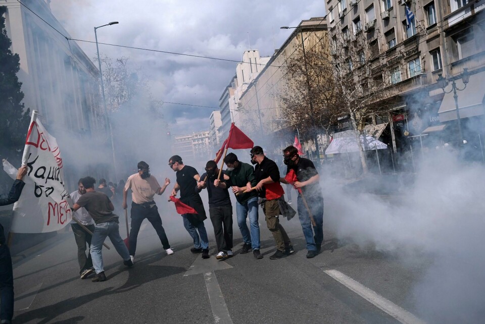 SINTE: Mange mennesker er sinte på myndighetene i Hellas. De demonstrerer etter en togulykke. Demonstranter forsøker å beskytte seg mot politiets tåregass under en protest søndag etter den voldsomme togulykken tirsdag. Foto: Aggelos Barai / AP / NTB