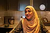 Golalah Abbasi står på kjøkkenet. Det er grå kjøkkenskap bak henne. Hun har på seg en beige hijab og en grønn blomstrete kjole.