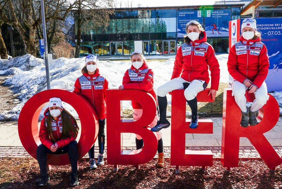 DEBUT: For første gang får damer delta i VM i kombinert. De som skal delta for Norge er (fra venstre): Hanna Midtsundstad, Mille Moen Flatla, Marte Leinan Lund, Mari Leinan Lund og Gyda Westvold Hansen. Bildet er av fem jenter i røde jakker. De sitter og lener seg på og i bokstavene O, B, E og R. De er skåret ut. Bildet er tatt i Oberstdorf i Tyskland. De har på munnbind.