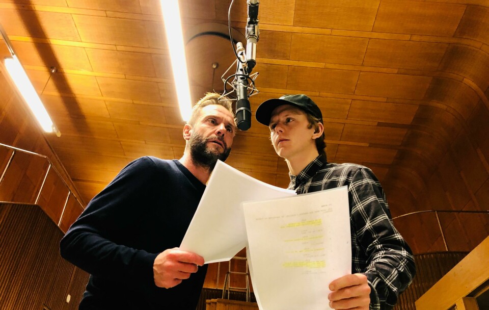 TEATER: NRK har laget radioteater i mange år. Noen år har de spilt inn krim-historier som du kan lytte til. Bildet er av skuespillerne Espen Reboli Bjerke og Jonas Strand Gravli. De står foran en mikrofon som henger ned foran dem. De holder i hvert sitt ark med manus.