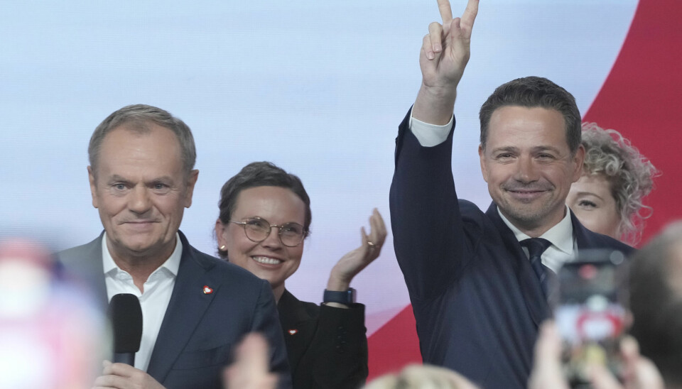 VALG: Rafal Trzaskowski (til høyre) viser to fingre i lufta under et valgarrangement. Ved siden av ham står Donald Tusk, leder for partiet Borgerplattformen. En mann i dress holder hånden i været og viser to fingre. Ved siden av ham står en annen mann med mikrofon, og to kvinner smiler i bakgrunnen. Publikum tar bilder.