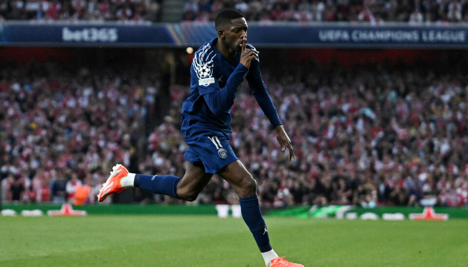 CHAMPIONS LEAGUE: Ousmane Dembélé jubler etter å ha scoret for PSG mot Arsenal i semifinalen i Champions League. En fotballspiller i mørkeblå drakt løper på gressbanen med høyre pekefinger foran munnen og hysjer på publikum. I bakgrunnen er det tusenvis av tilskuere på tribunen.