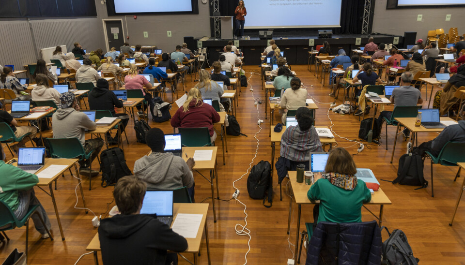 EKSAMEN: Elever gjennomfører eksamen på videregående skole. Neste år starter eksamen én uke tidligere enn før. Elever sitter ved pulter i en stor sal og jobber på bærbare datamaskiner under en eksamen. Ledninger til strøm ligger på gulvet.