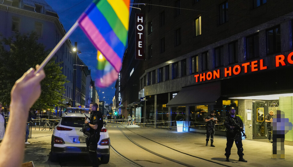 KRIMINALITET: Politiet sperrer av området rundt London Pub og Per på Hjørnet etter terrorangrepet 25. juni 2022. En person holder opp en regnbueflagg. I bakgrunnen står politiet med våpen utenfor Thon Hotel Rosenkrantz i Oslo.