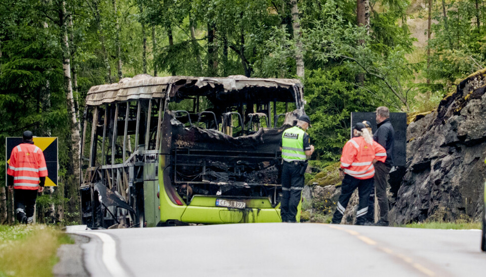 BRANN: Bussen ble helt ødelagt etter brannen. Tre personer ble kritisk skadd. En utbrent grønn buss står på en vei omgitt av skog. Rundt bussen er det politi og annet redningsmannskap.
