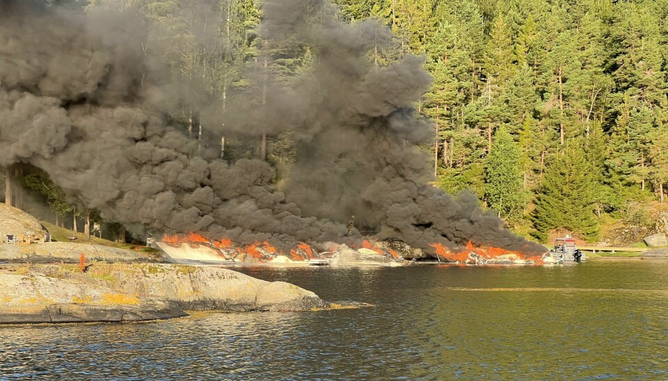 OPPSLUKT: Syv båter var slukt av flammene da nødetatene kom til Skutevikkilen på Kragerø. Bildet viser viken hvor flere båter står i flammer. Sort røyk stiger opp fra båtene og kaien