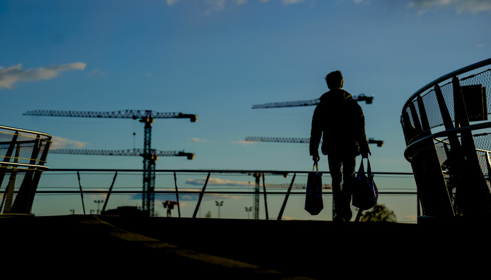 RISIKO: Byggebransjen er den med mest a-krim, ifølge fagbladet Fri Fagbevegelse. Lovbruddene får mest i lønnstyveri og dårlige boforhold. Bildet viser en byggeplass med flere heisekraner. En person går foran. Det er mørkt og vi ser bare siluetter.